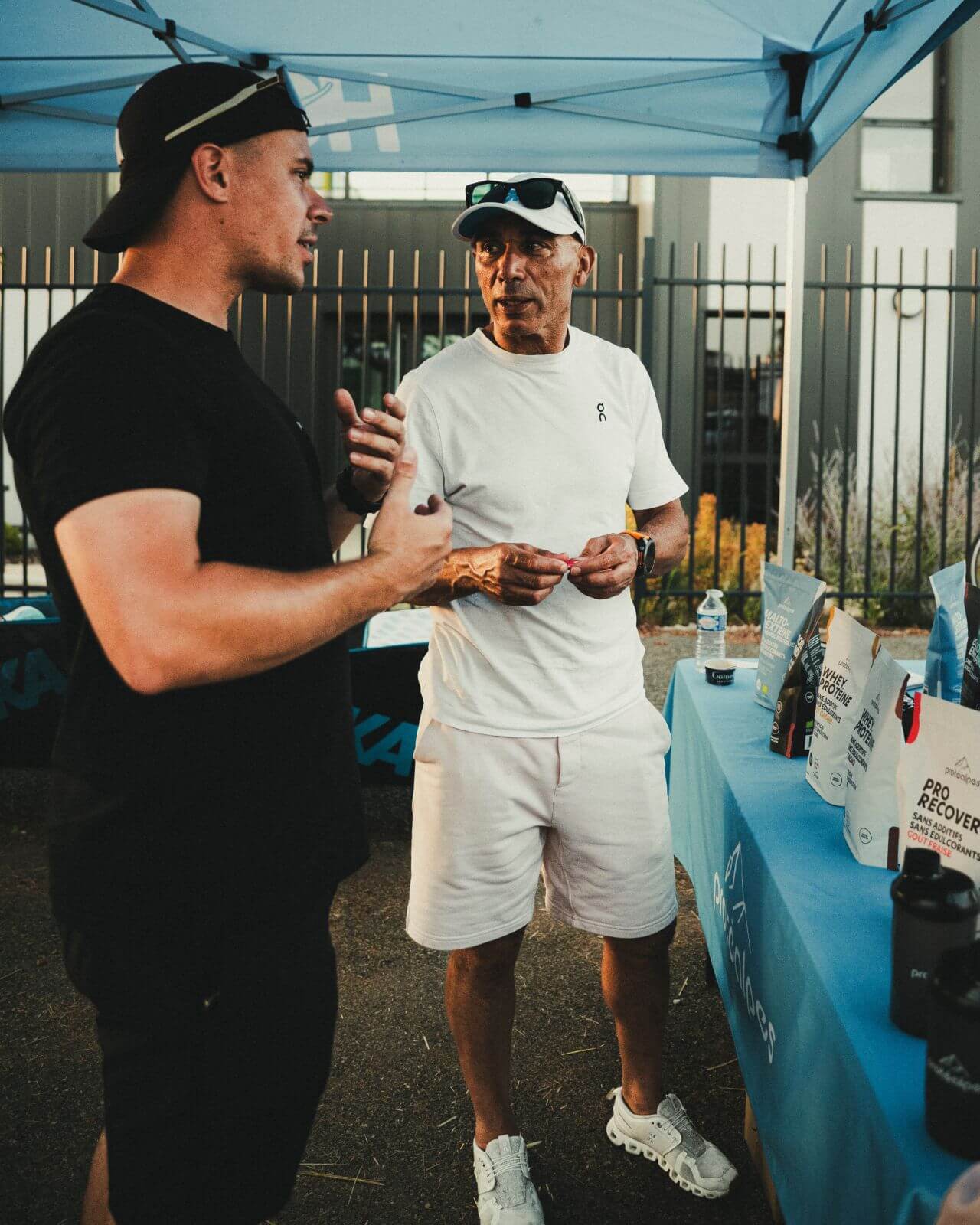 Deux hommes discutent sous un stand Protéalpes, entourés de produits de nutrition sportive sans édulcorants ni additifs.