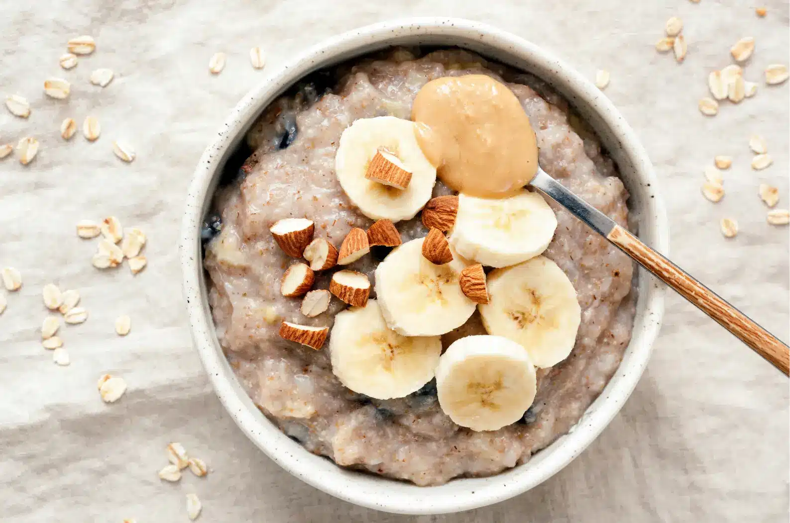 Bol de porridge aux bananes et amandes, orné de beurre de cacahuète. Nutrition sportive Protéalpes, sans additifs.