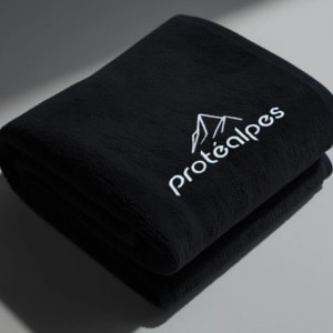 Serviette en tissu noir avec logo Protéalpes, représentant notre engagement envers la nutrition sportive sans additifs ni édulcorants.