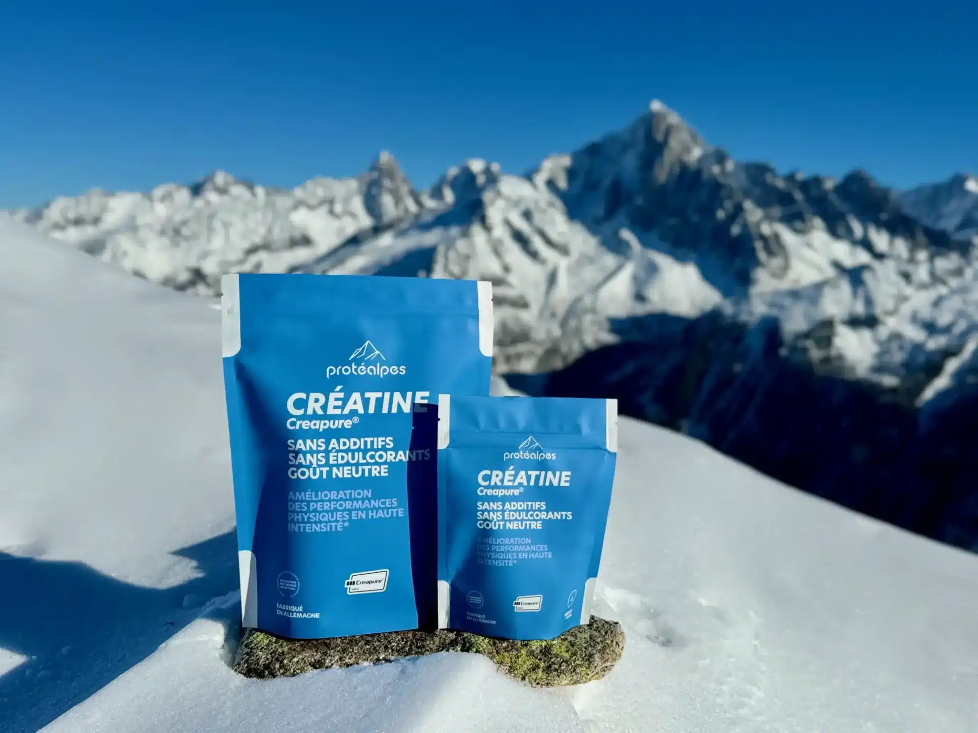 Sachets de créatine Protéalpes sans additifs ni édulcorants, posés sur la neige avec vue sur les montagnes en arrière-plan.