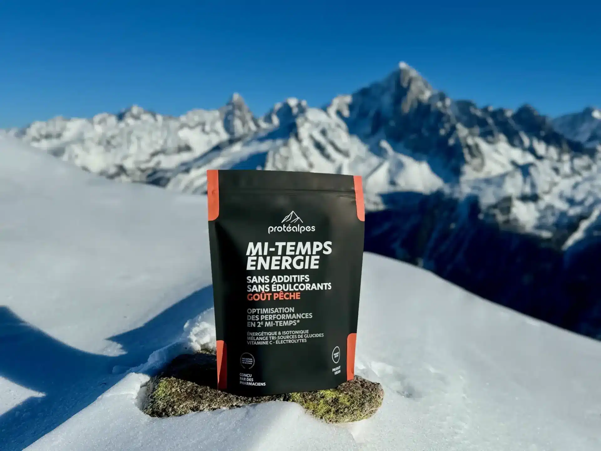Pack de Protéalpes Mi-Temps Énergie sans additifs ni édulcorants, posé sur neige avec montagnes en arrière-plan.