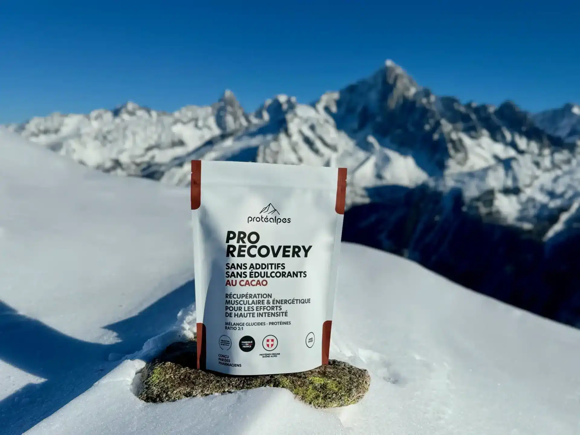Produit de récupération ProtéAlpes sur neige, sans additifs ni édulcorants, avec montagnes en arrière-plan.