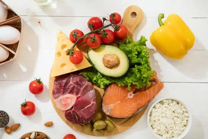 Plateau coloré d'aliments frais: avocat, fromage, saumon, viande, légumes verts et œufs. Nutrition sportive sans additifs.
