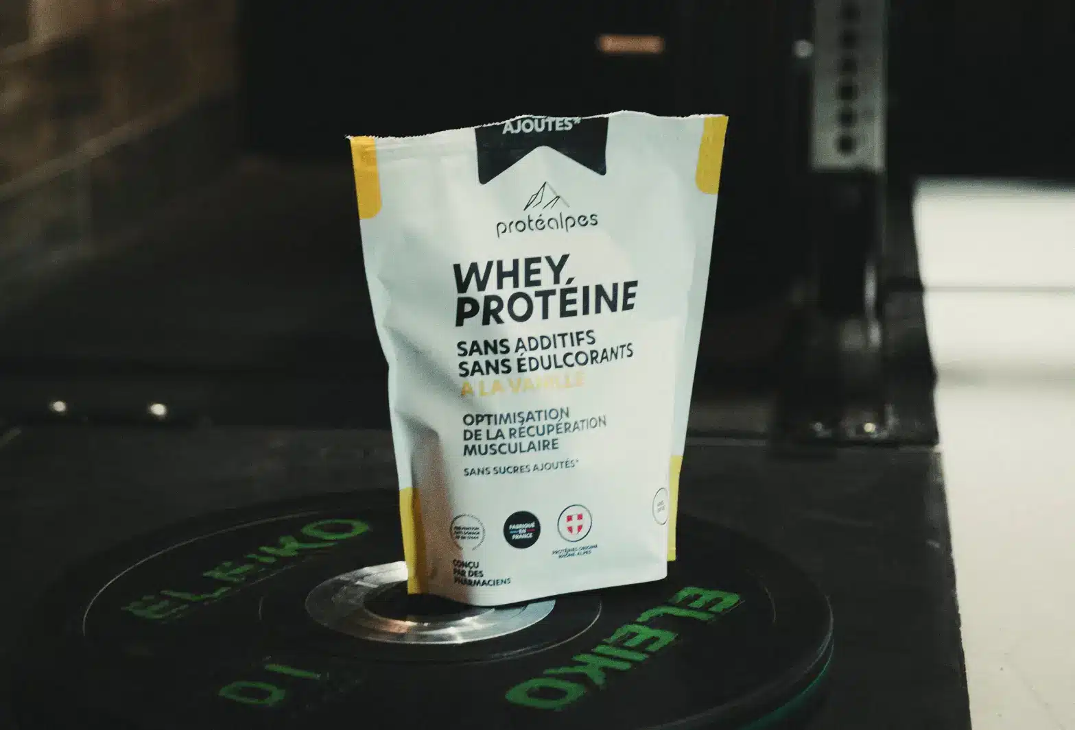 Protéines Protéalpes vanille, sans additifs ni édulcorants, sur un disque de musculation, pour une nutrition sportive pure.