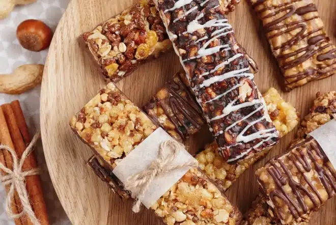 Barres granola Protéalpes, sans édulcorants ni additifs, présentées sur une assiette en bois, entourées de noisettes et cannelle.
