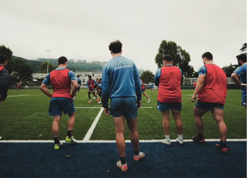 Groupe de rugby en entraînement sur terrain, portant les couleurs Protéalpes, symbole de nutrition sportive sans édulcorants.